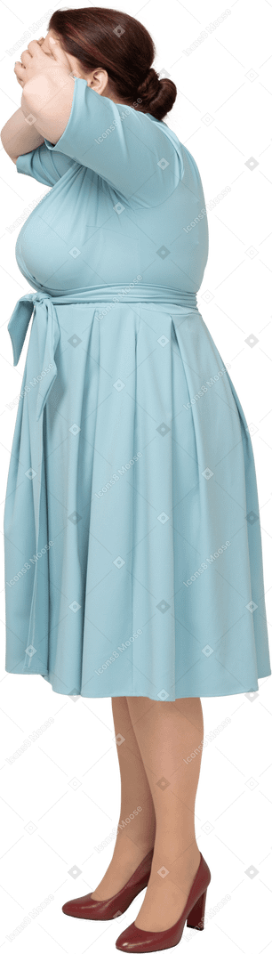 Side view of a woman in blue dress covering eyes with hands