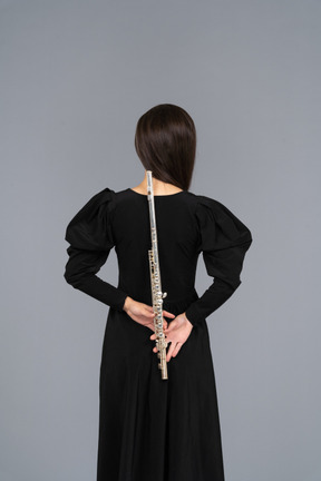 Back view of a young lady in black dress holding flute behind