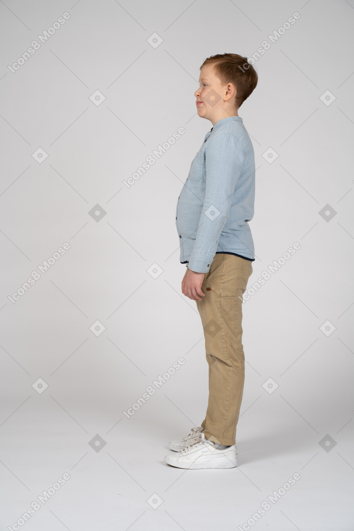 Side view of a boy in casual clothes standing still and making faces