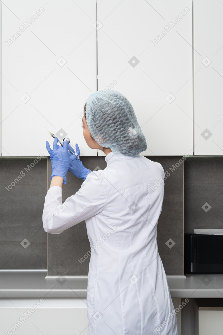 Vista traseira de uma enfermeira com um chapéu de médico segurando uma seringa e olhando para o lado
