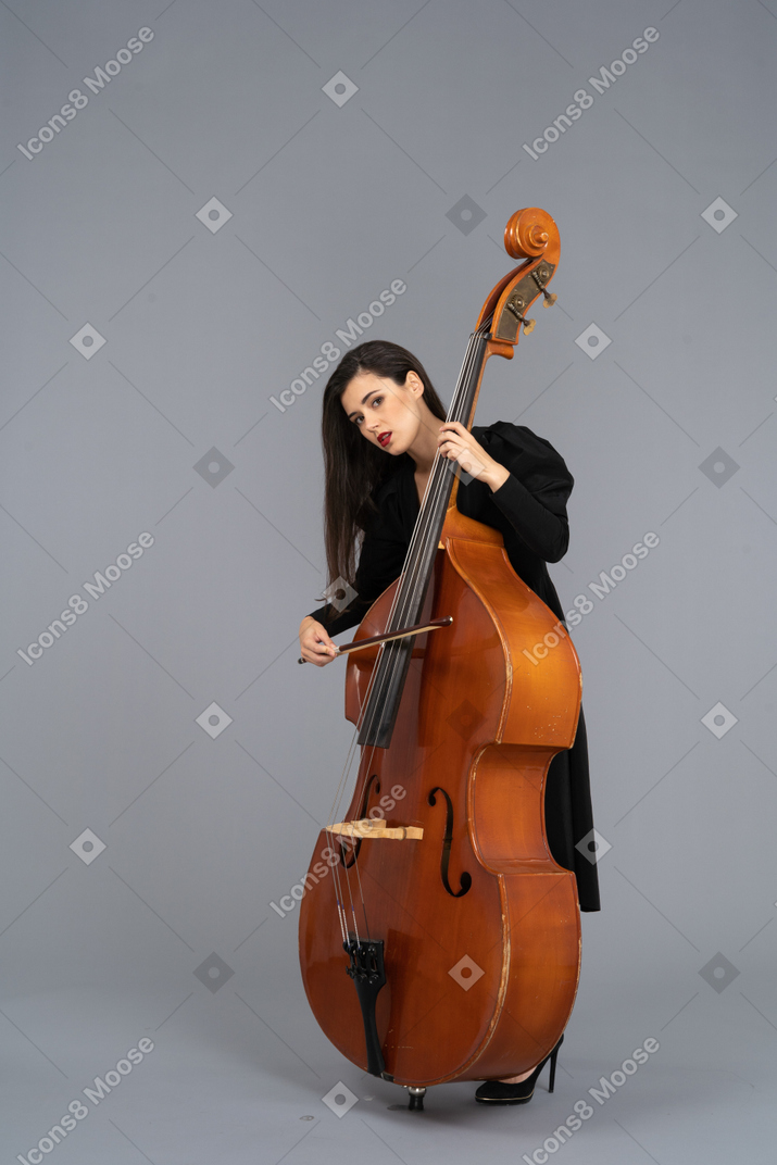 弓でコントラバスを演奏する黒いドレスを着た若い女性の4分の3のビュー