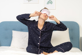 Vista frontal de una joven en pijama poniéndose máscara para dormir