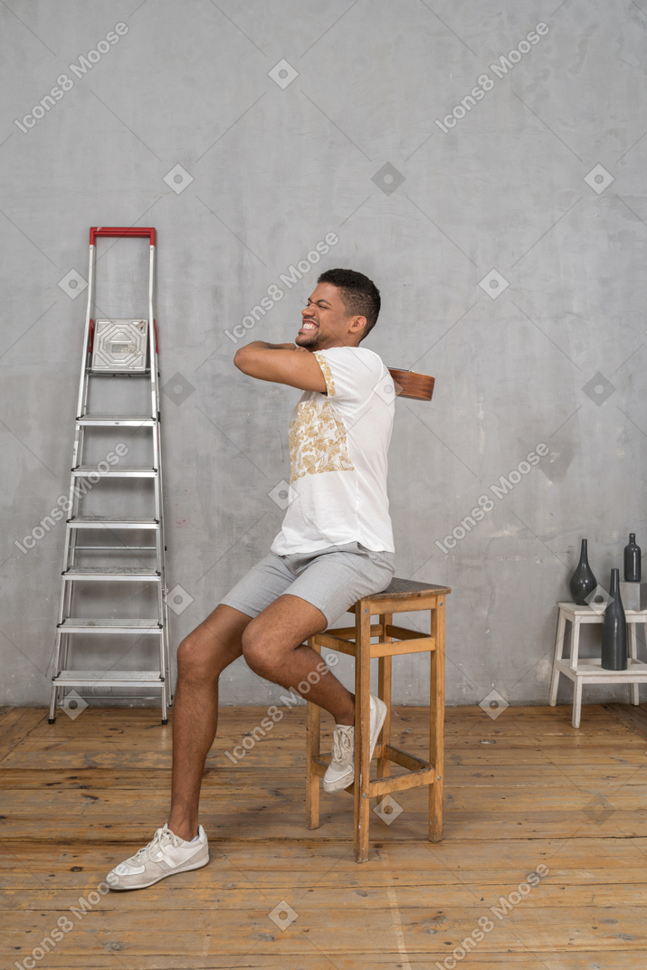 Vista de tres cuartos de un hombre en un taburete balanceando un ukelele y burlándose