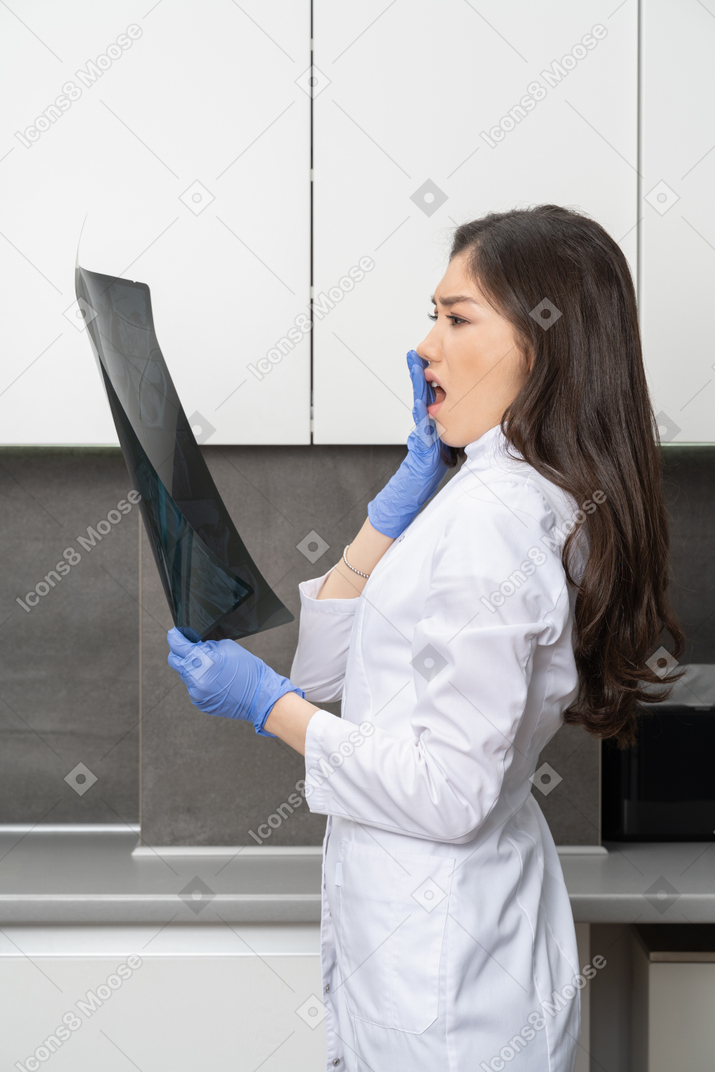 Side view of a shocked female doctor looking at x-ray image and hiding her mouth
