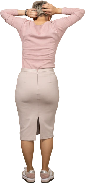 Rear view of a woman in casual clothes standing with hands behind head