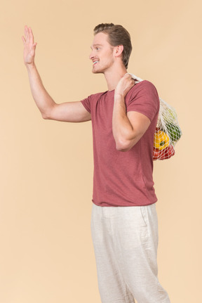 Young guy holding a string bag with groceries and waving