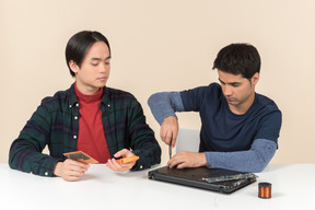 Zwei junge aussenseiter sitzen am tisch und haben probleme mit der reparatur des laptops