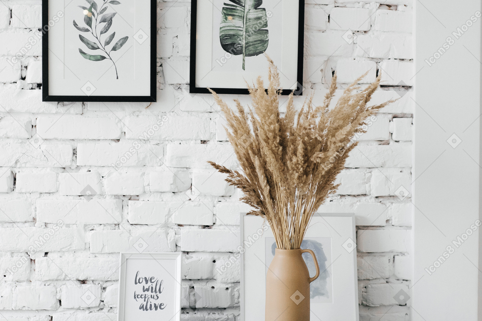 A vase filled with dry grass next to pictures on a wall