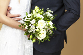 Braut und bräutigam, die einen hochzeitsblumenstrauß halten