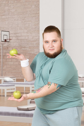 A fat man holding two green apples in his hand
