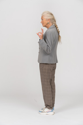 Vista lateral de una anciana en traje mostrando signo ok