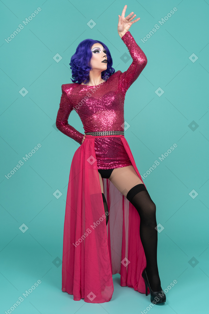 Drag queen in pink dress reaching their hand up & putting foot forward