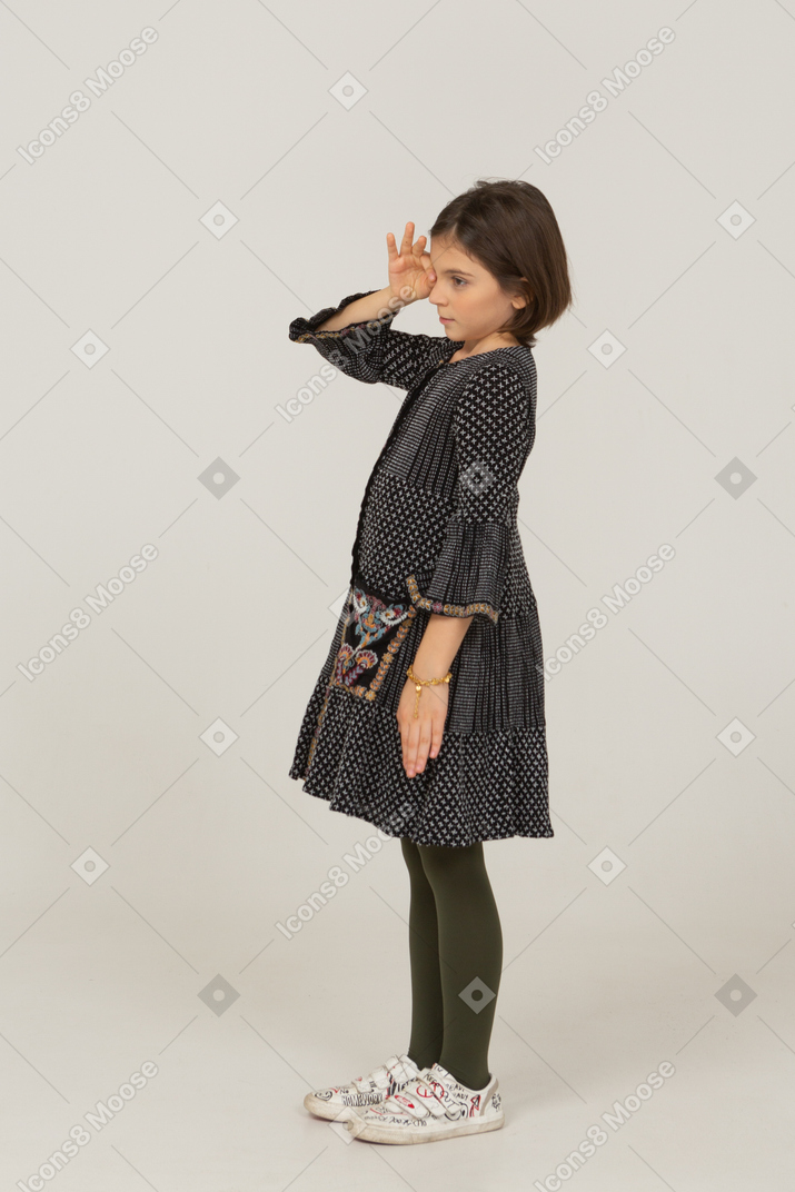 Side view of a little girl in dress watching through the fingers
