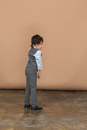 Vista traseira de um menino de terno cinza, olhando para a câmera