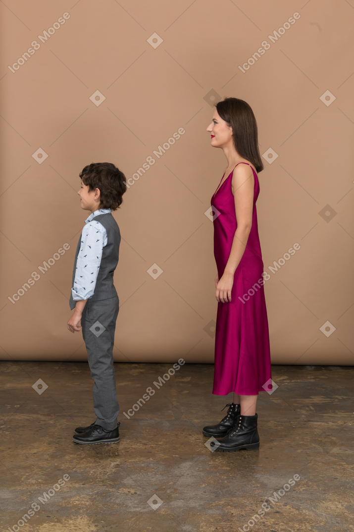 Stylsih mujer en vestido rojo y niño en traje chaleco de pie en el perfil