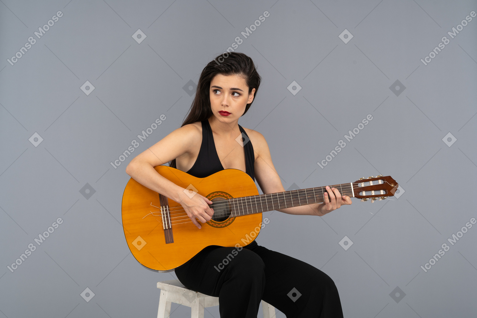 Vorderansicht einer sitzenden jungen dame im schwarzen anzug, die gitarre spielt und beiseite schaut