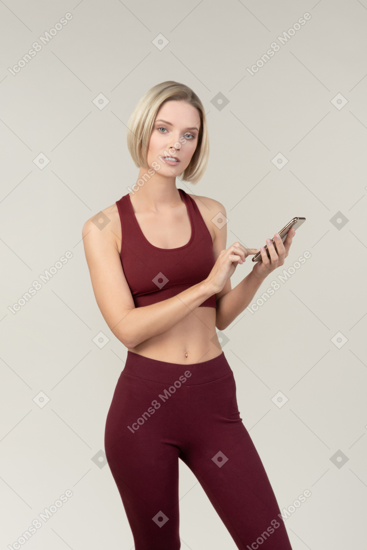Молодая женщина в спортивной одежде с помощью телефона