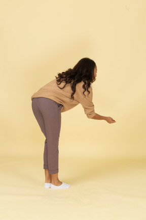 Three-quarter back view of a dark-skinned young female bending down and outstretching hand