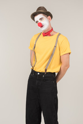 Sad male clown standing with hands behind the back