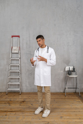 Three-quarter view of a young gesticulating doctor standing in a room with ladder and chair