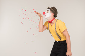 Male clown standing in profile and blowing confetti