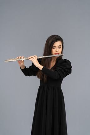 フルートを演奏する黒いドレスを着た真面目な若い女性の正面図