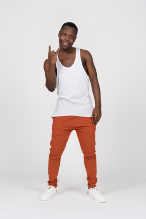 Front view of smiling young man looking at camera and showing the sign of the horns