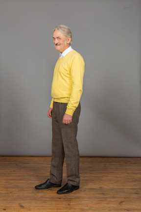Dreiviertelansicht eines alten fröhlichen mannes im gelben pullover, der lächelt und kamera betrachtet