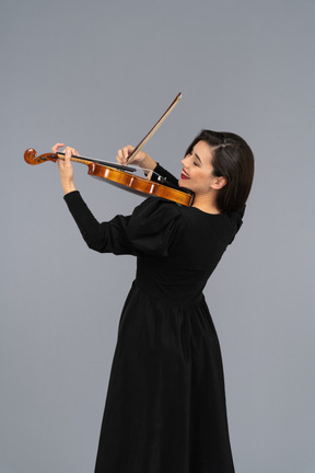 Close-up de uma jovem alegre de vestido preto tocando violino