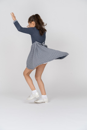 Three-quarter back view of a girl dancing with hands up in the air
