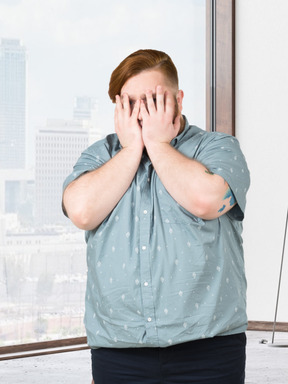 Man standing in a room and covering his face