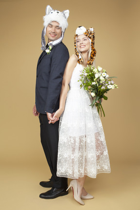 Noivo e noiva usando chapéus animais e de mãos dadas