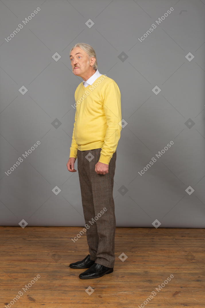 Vista de três quartos de um homem idoso em um pulôver amarelo mostrando a língua