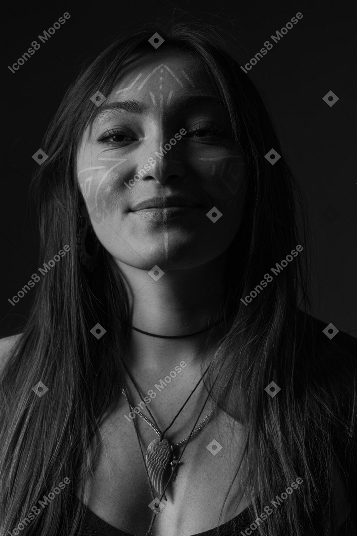 Front view noir picture of a young female with face art looking aside