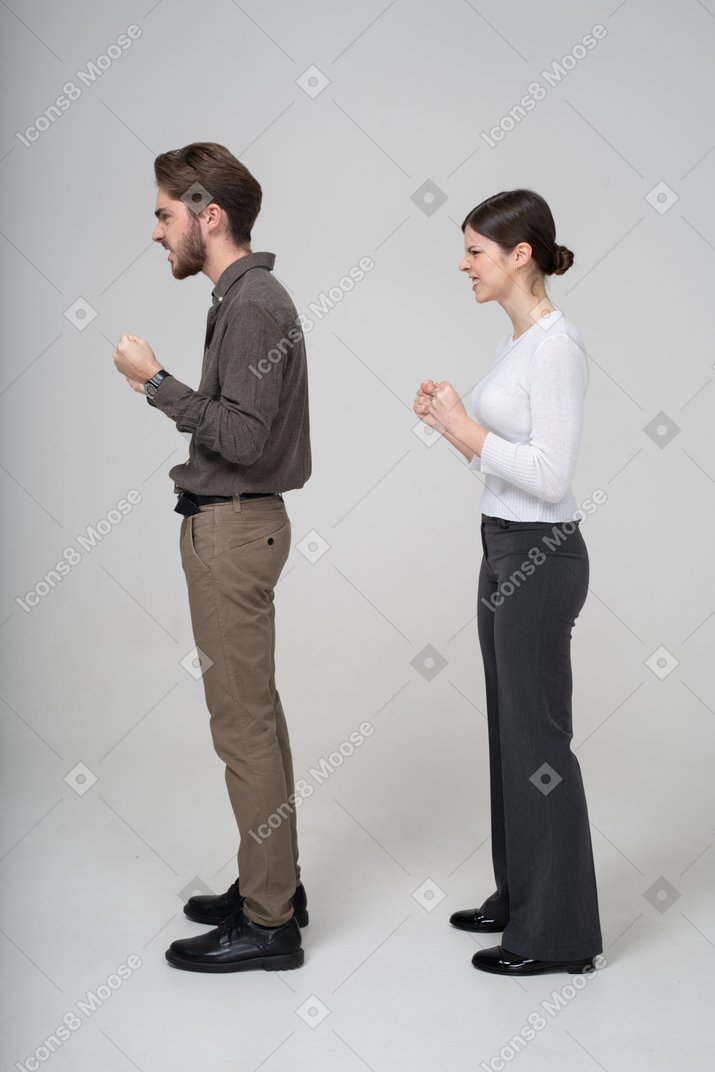 一对愤怒的夫妻在办公服装紧握拳头的侧视图