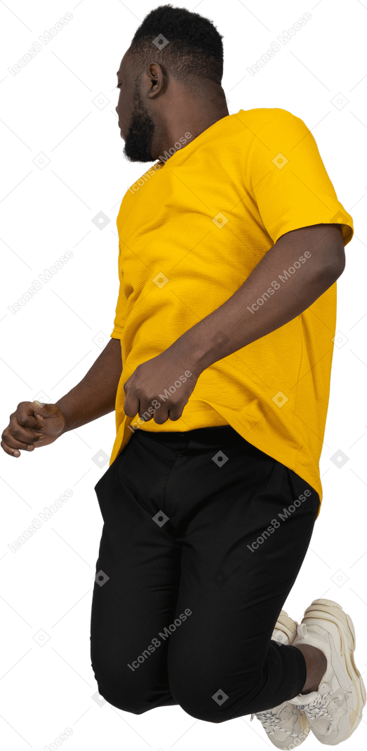 Vista de três quartos de um jovem de pele escura pulando em uma camiseta amarela