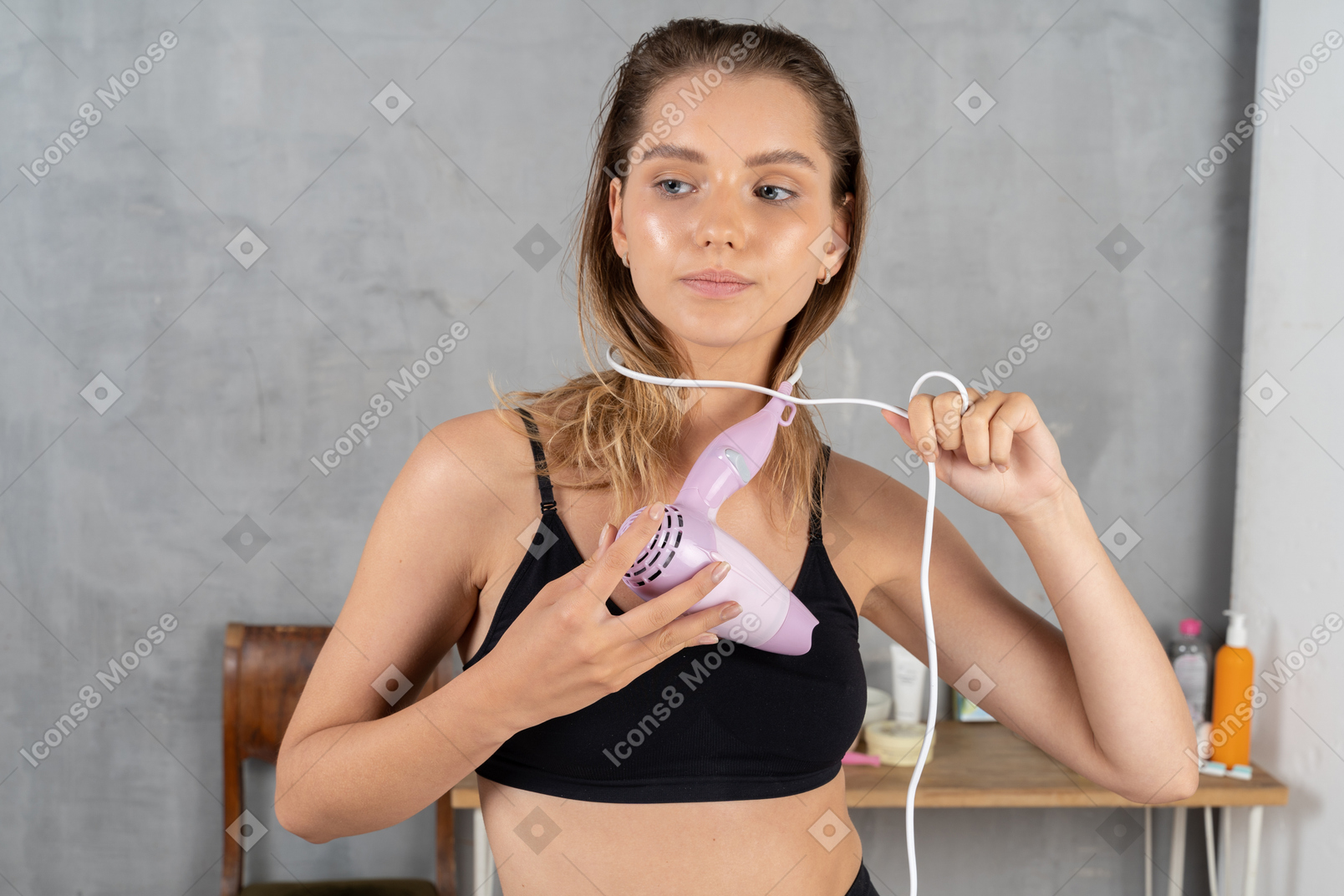Front view of a young woman wrapping a hairdryer cord around her neck