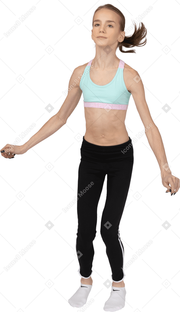Vista frontal de una jovencita en ropa deportiva bailando mientras mira directamente