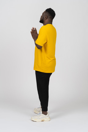 Vista lateral de um jovem de pele escura em uma camiseta amarela de mãos dadas