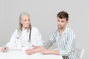 Doctora de edad revisando la presión sanguínea de un joven