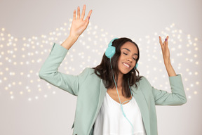 Mujer joven bailando con auriculares frente a la pared con luces de guirnalda