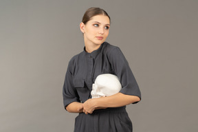 Front view of a young woman in a jumpsuit holding a plaster skull