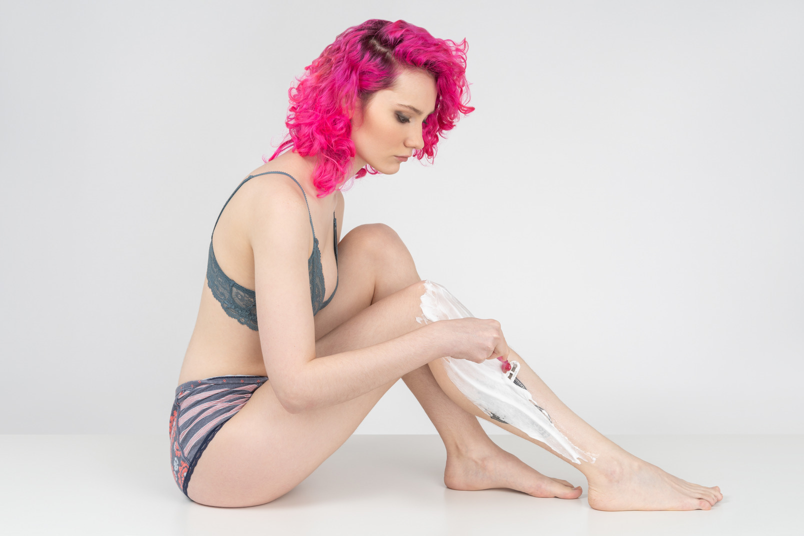 Young woman with curly pink hair shaving legs