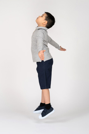 Мальчик прыгает с распростертыми руками в профиль