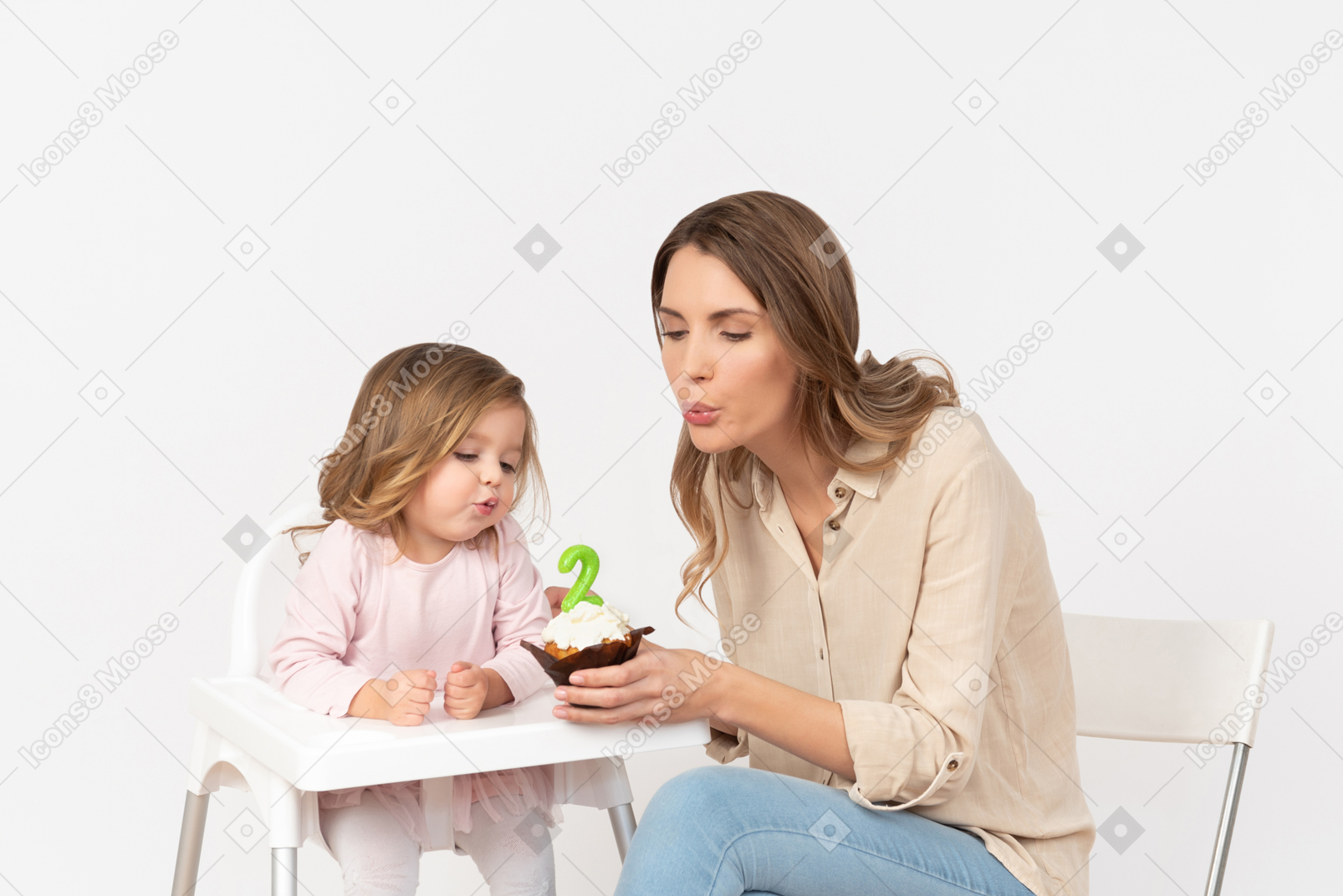 Baby girl blowing out a candle as her mother's holding a birthday cake