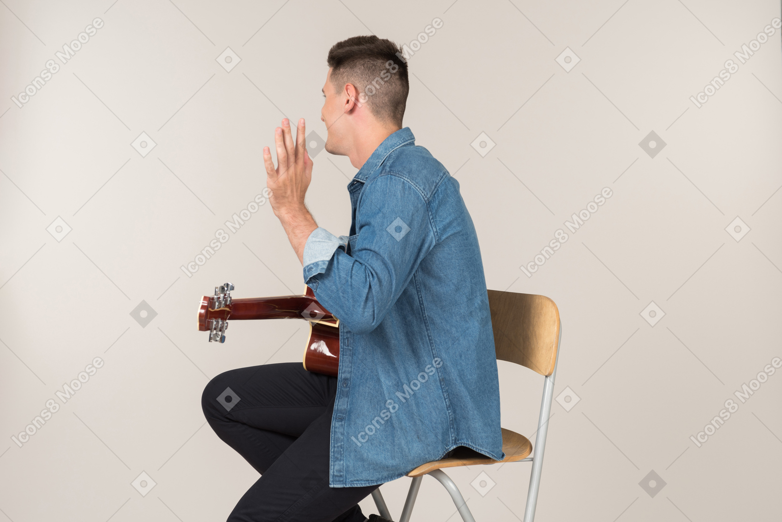 Young guy sitting on the table in profile and playing on guitar