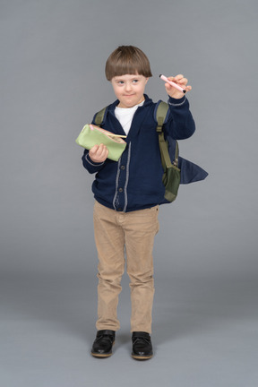 Little boy with a backpack holding up a pen