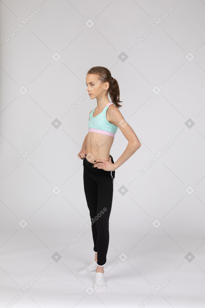 Vista de tres cuartos de una jovencita en ropa deportiva poniendo las manos en las caderas