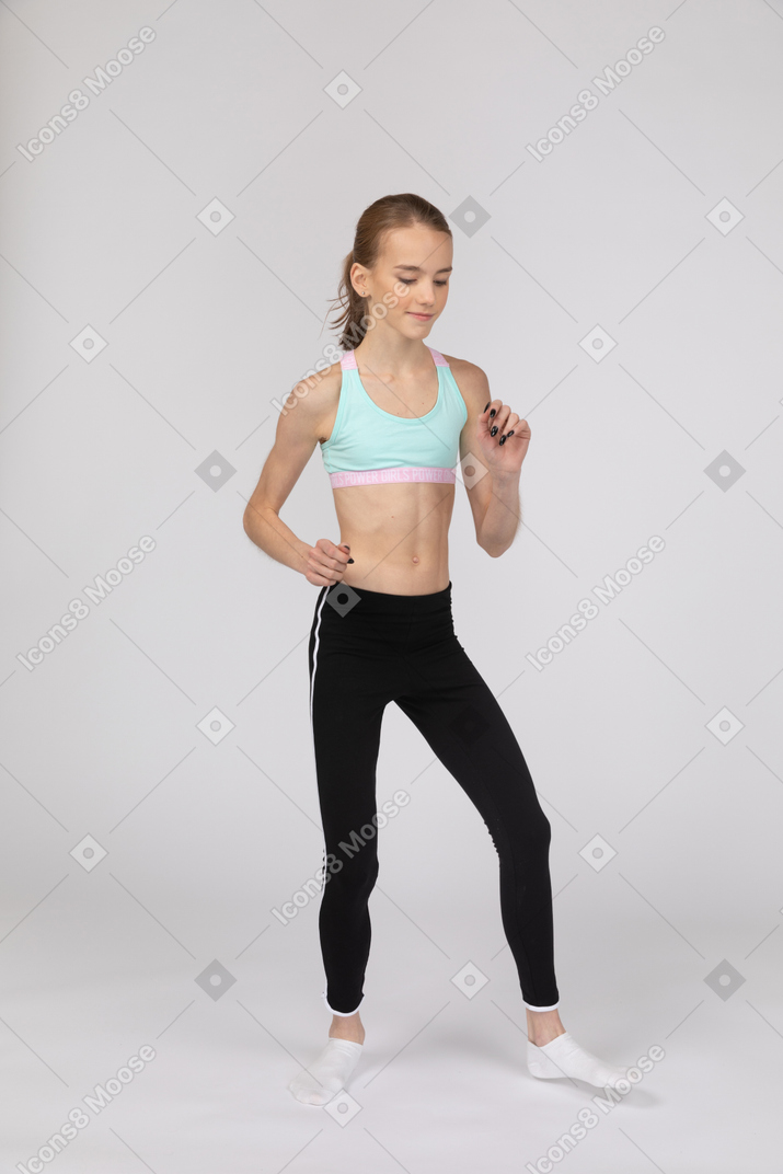 Vista de três quartos de uma adolescente em roupas esportivas, caminhando e levantando o braço