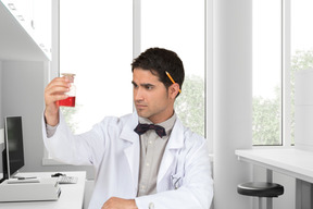 Jovem cientista segurando um tubo de ensaio com algo vermelho na mão